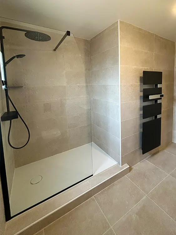 Cette rénovation privilégie l'accessibilité, le confort d'utilisation et la simplicité d'entretien grâce à une douche spacieuse et des équipements modernes. Projet réalisé par Grech Salle de Bain sur le secteur de Sanary-sur-Mer et de l'agglomération toulonnaise. Salle de bain rénovée avec douche contemporaine, receveur extra-plat et sèche-serviettes noir