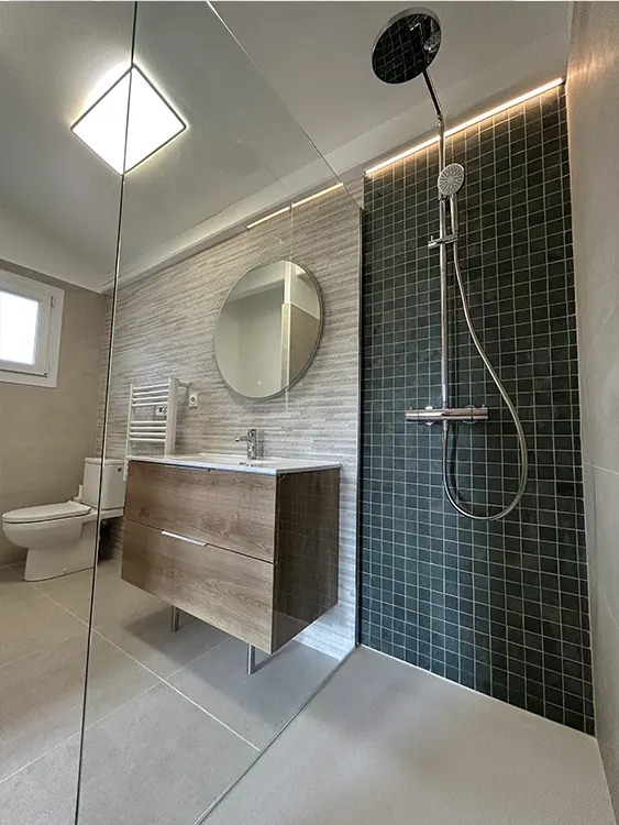 Douche contemporaine réalisée à Sanary-sur-Mer avec receveur blanc, paroi vitrée fixe, colonne de douche à effet pluie, mosaïque verte et carrelage mural gris-beige. Douche spacieuse avec receveur blanc et paroi vitrée