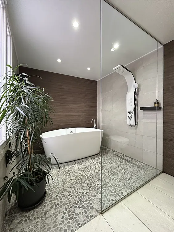 Rénovation d'une salle de bain à Sanary-sur-Mer avec baignoire îlot, douche vitrée, sol effet galets et revêtements muraux imitation bois. Salle de bain contemporaine avec baignoire et douche