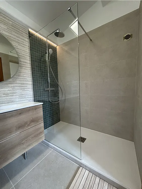 Aménagement d'une salle de bain à Sanary-sur-Mer avec douche vitrée, mosaïque murale vert foncé, colonne de douche chromée, meuble vasque effet bois et éclairage LED. Douche contemporaine avec mosaïque vert foncé